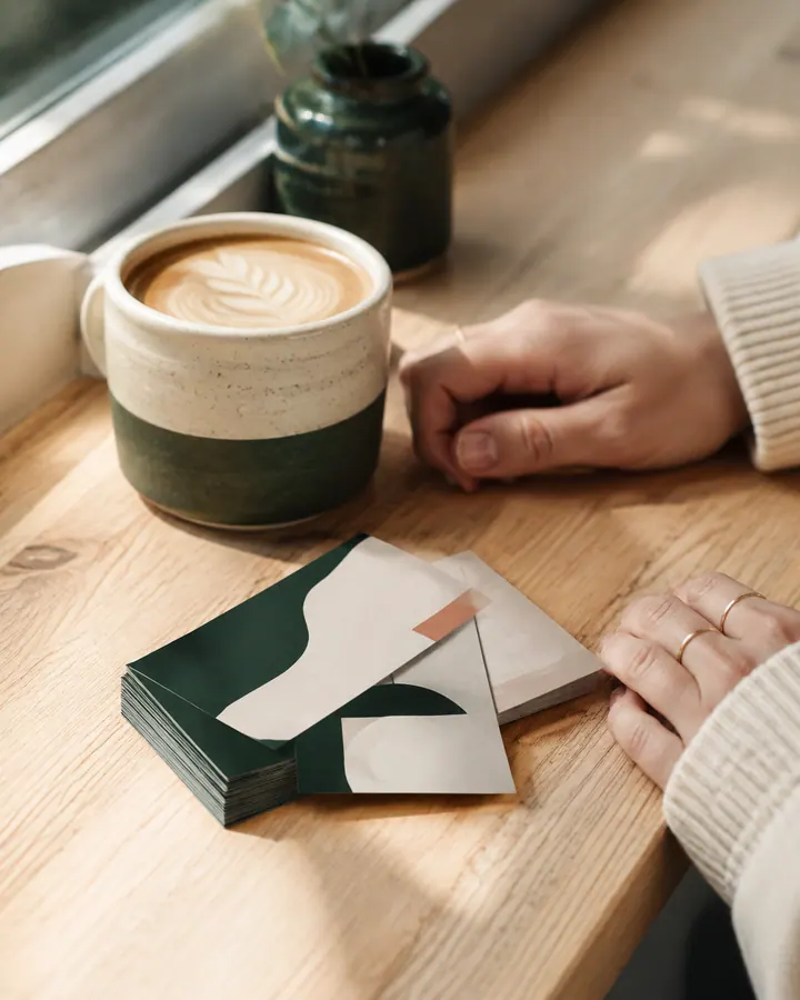 Abstract green and cream business cards on a sunlit café counter